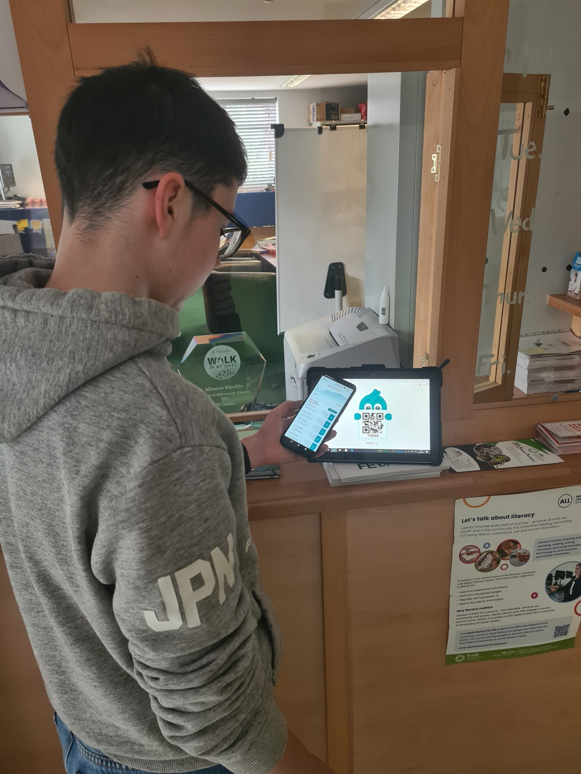 Male teenager standing with a phone in front of an iPad showing a QR code